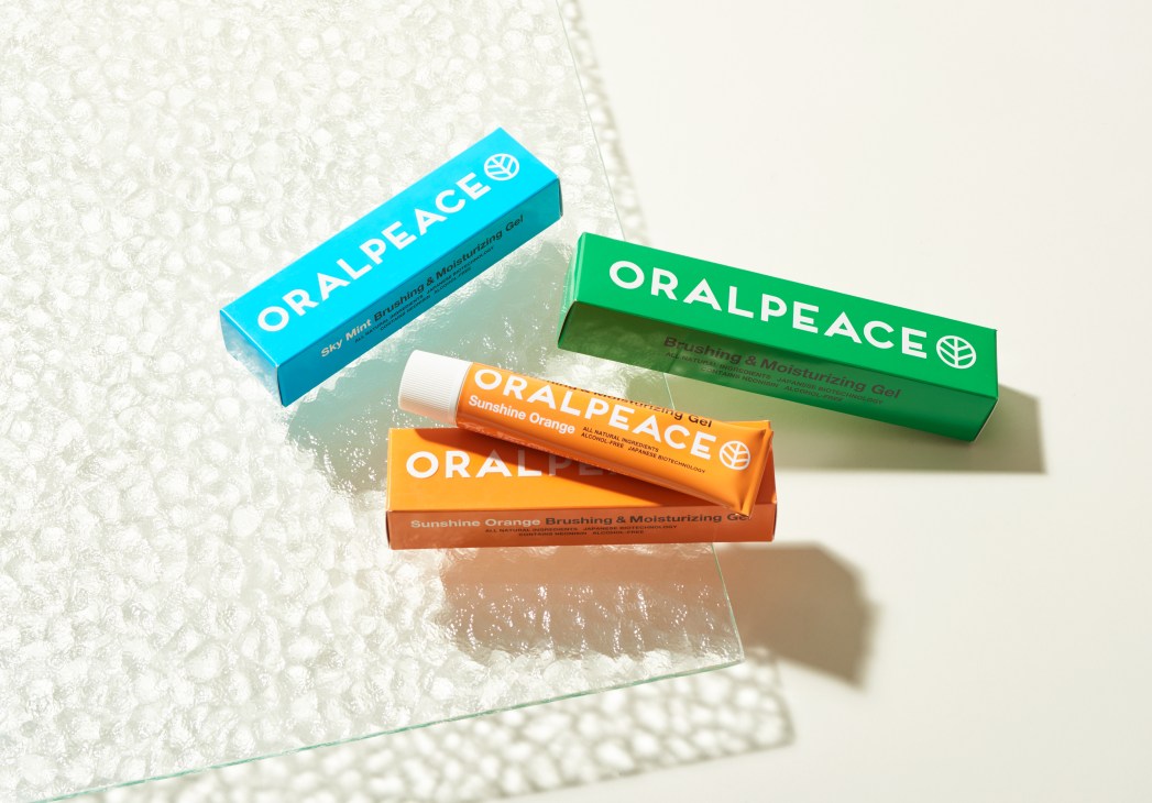 Three Oralpeace toothpaste tubes in blue, green, and orange packaging displayed on a textured white surface.