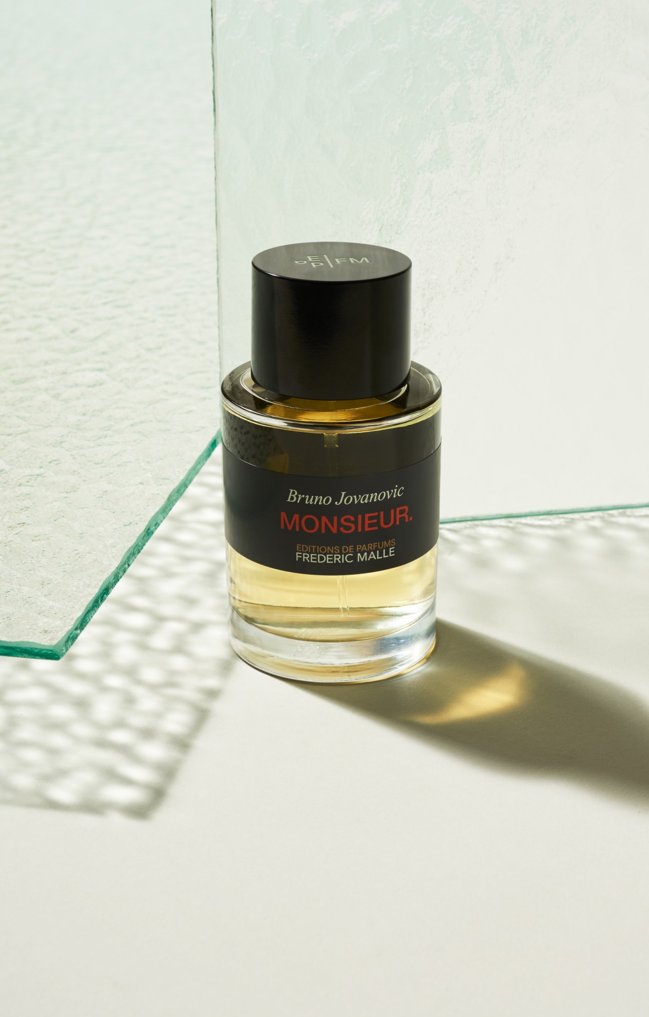 Frédéric Malle Monsieur perfume bottle with black cap on white surface with green glass edge.