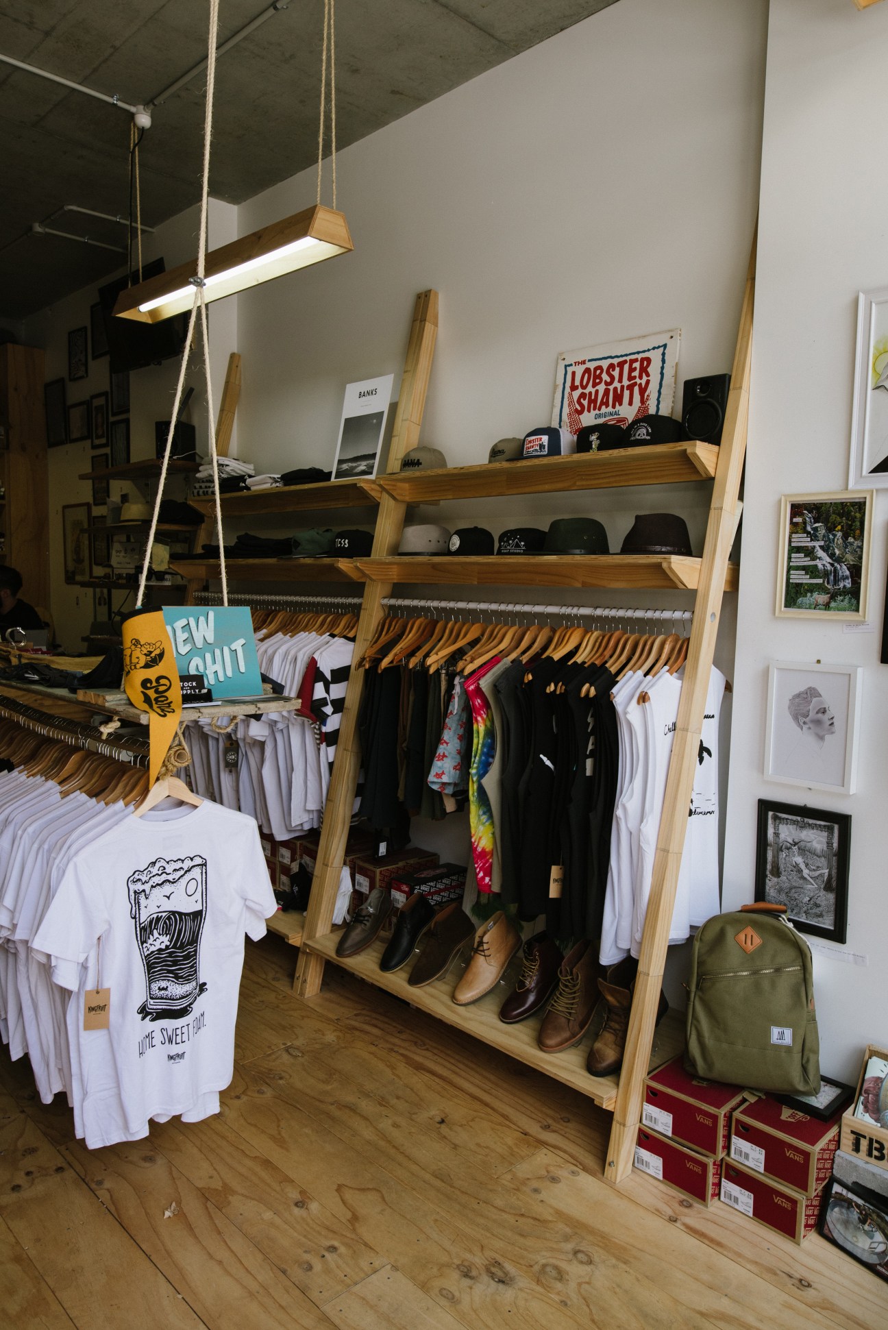 Interior of Stock & Supply concept store displaying wooden clothing racks with shirts and shoes, shelving with caps and merchandise.
