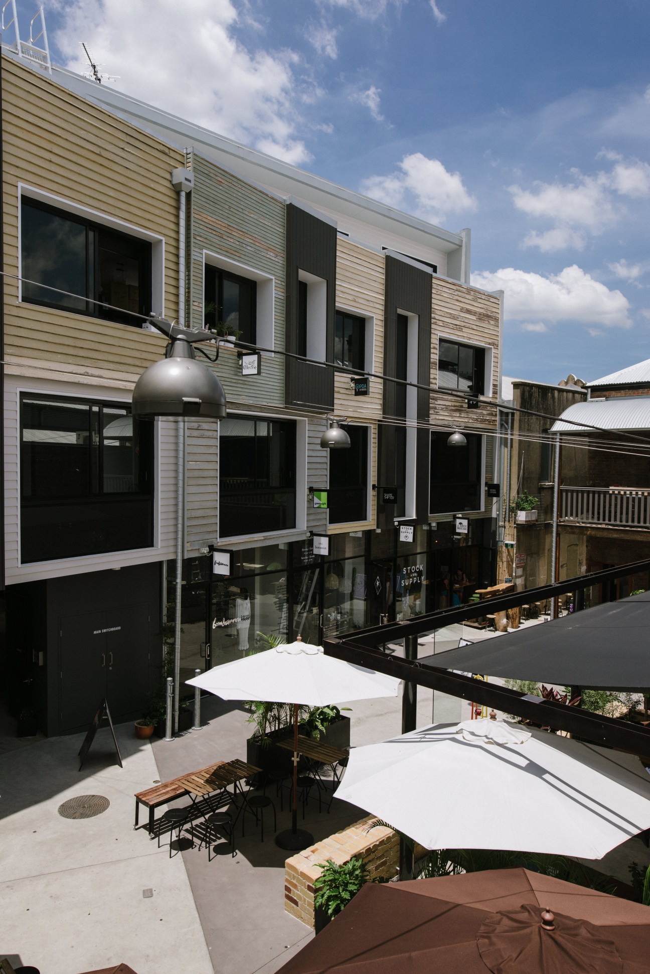 Bakery Lane courtyard with retail storefronts, white umbrellas, and seating areas on a sunny day.