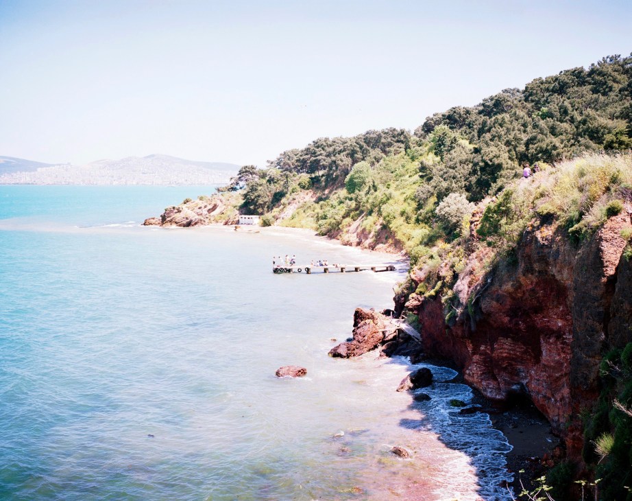Verdant cliffs overlook a sandy beach with turquoise water and boats on Heybeliada in the Princes' Islands.