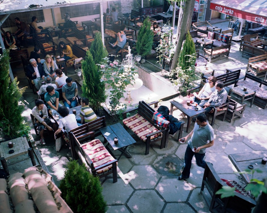 Overhead view of Lalezar Café's rooftop terrace with cypress trees, wooden benches, and patrons dining in Istanbul's Maltepe district.