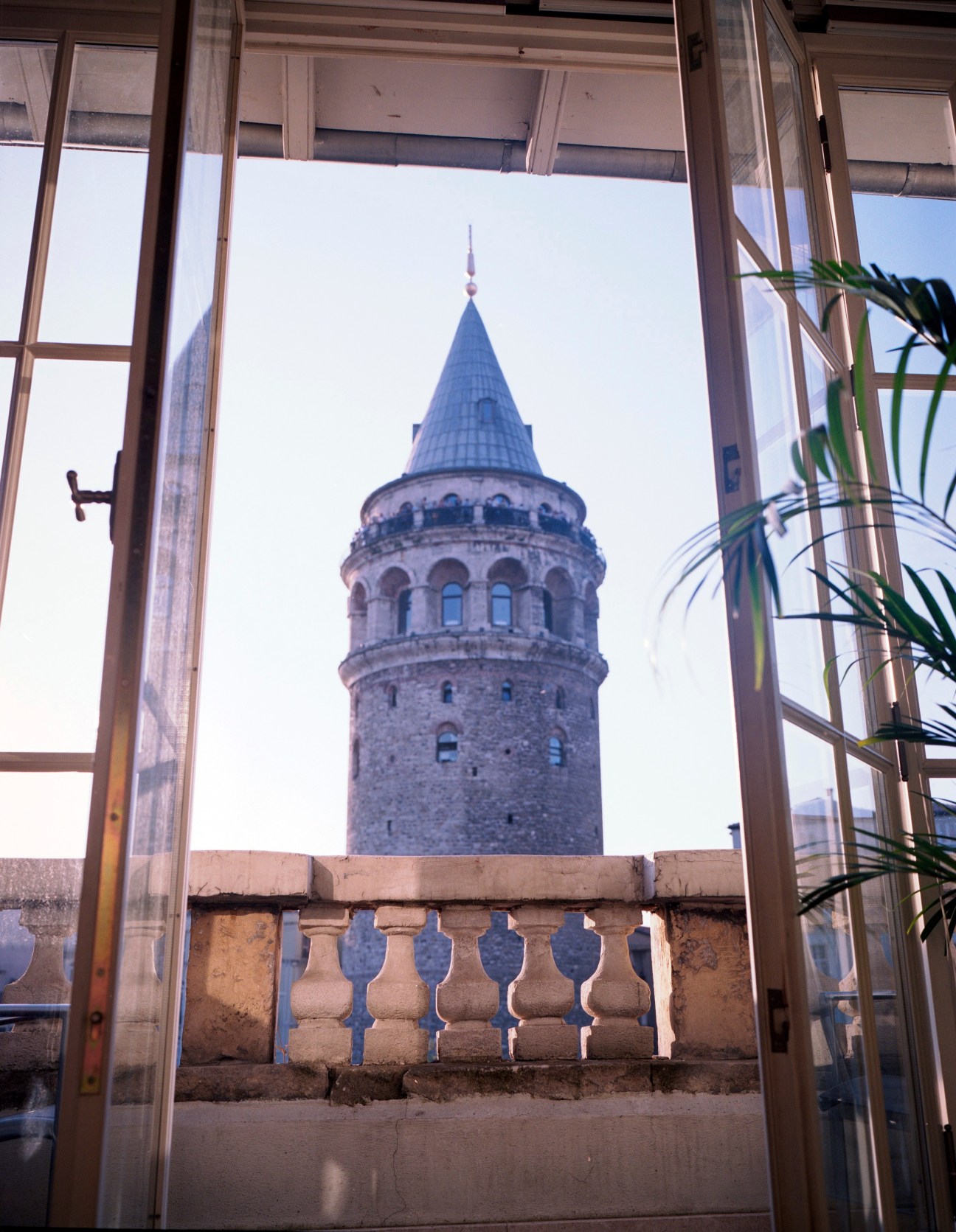 Galata Tower viewed through open windows from a private residence, with potted plant in foreground.