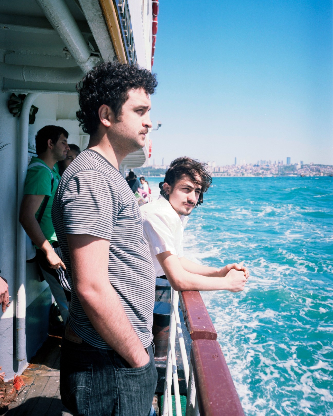 Passengers on the Kadıköy ferry gazing at the Bosphorus with Istanbul skyline in the background.