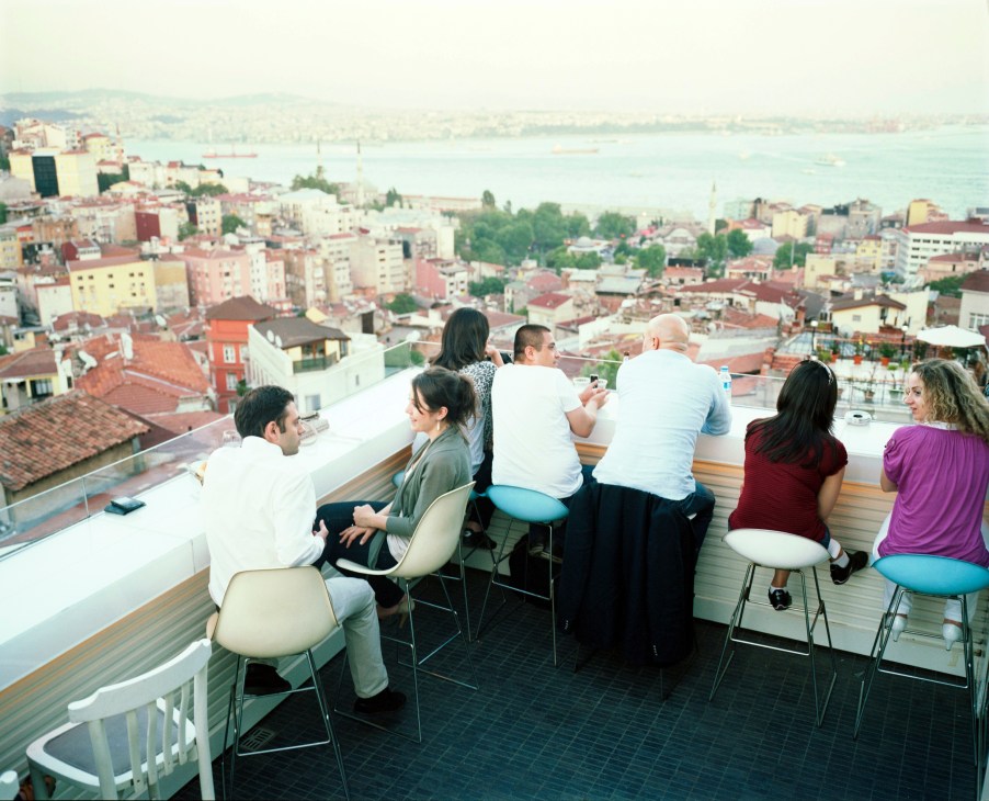 People sitting on a rooftop bar overlooking Istanbul's cityscape and the Bosphorus strait.