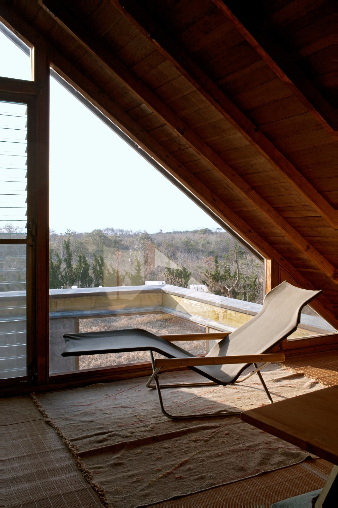 Third-floor workspace with wooden beam ceiling, large windows overlooking forested landscape, and a folding chaise lounge by Takeshi Nii.
