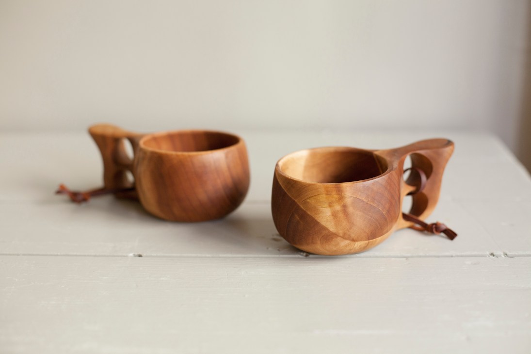 Two handcrafted wooden bowls with handles displayed on a white surface.