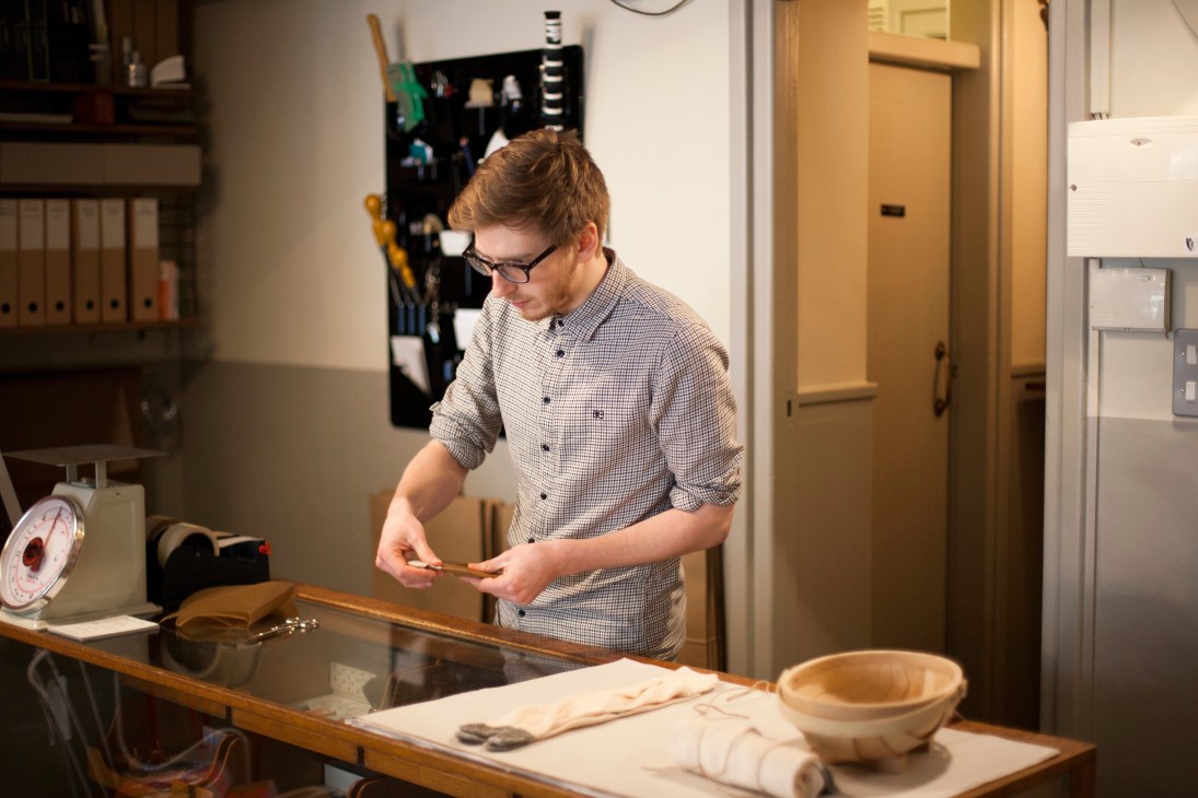 Man in checked shirt examining wooden object at counter in design store.