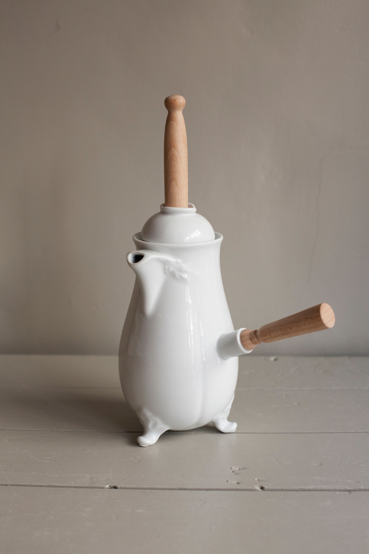 White ceramic vessel with wooden handles and plunger, displayed against a neutral background.