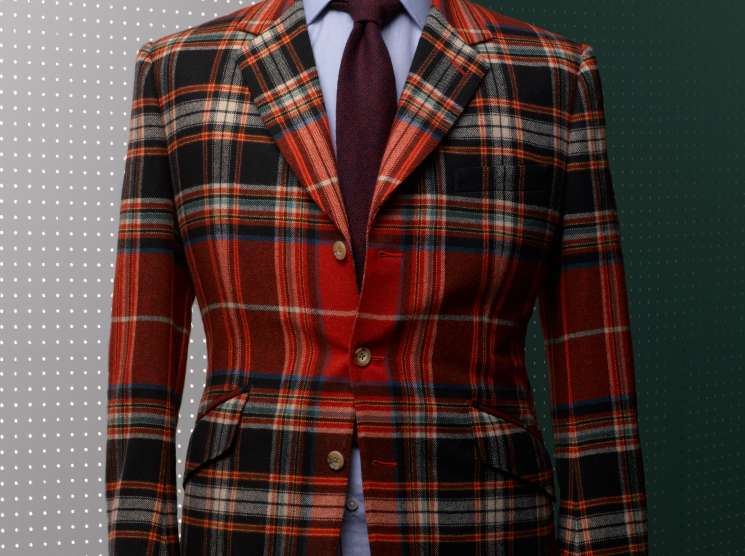 Red and black tartan blazer with burgundy tie displayed on a dress form against a two-tone background.