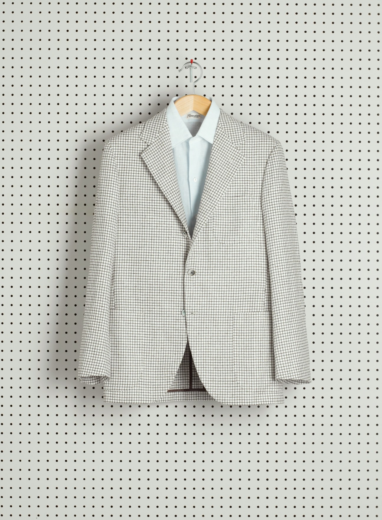 Checkered blazer on wooden hanger against perforated white background.