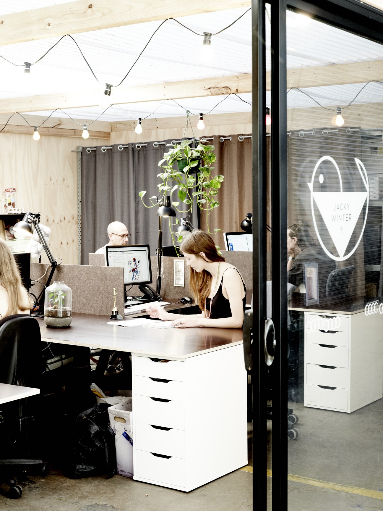 Interior of The Jacky Winter Group offices with staff working at desks under exposed wooden beams and pendant lighting.