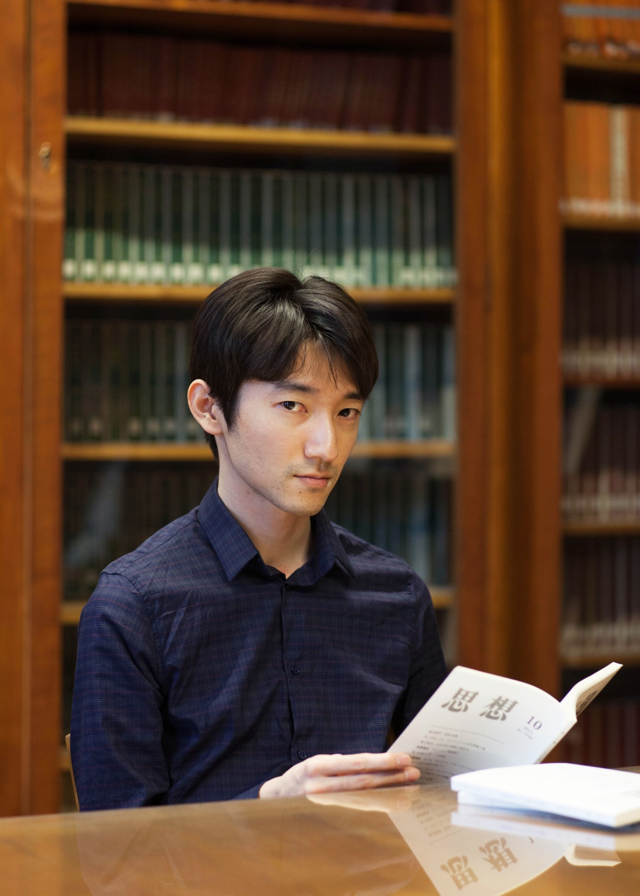 Student reading a Japanese publication in the library at Maison du Japon with bookshelves behind him.