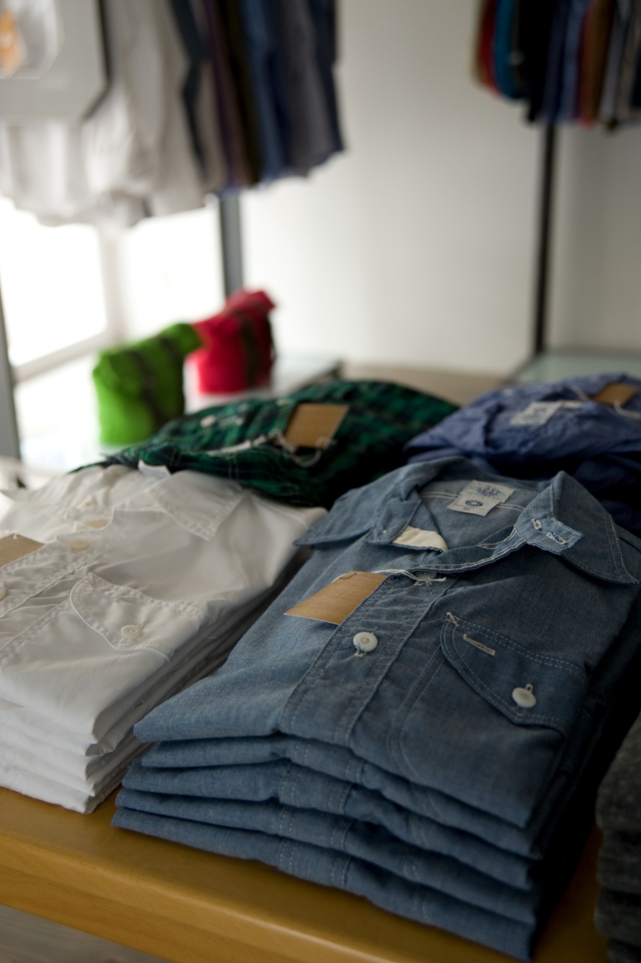 Folded denim shirts and jackets with brown leather labels displayed on a table in a retail setting.