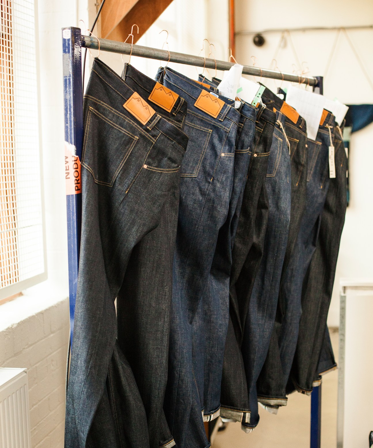 Finished jeans hanging on a rail with orange leather labels at Blackhorse Lane Ateliers factory.