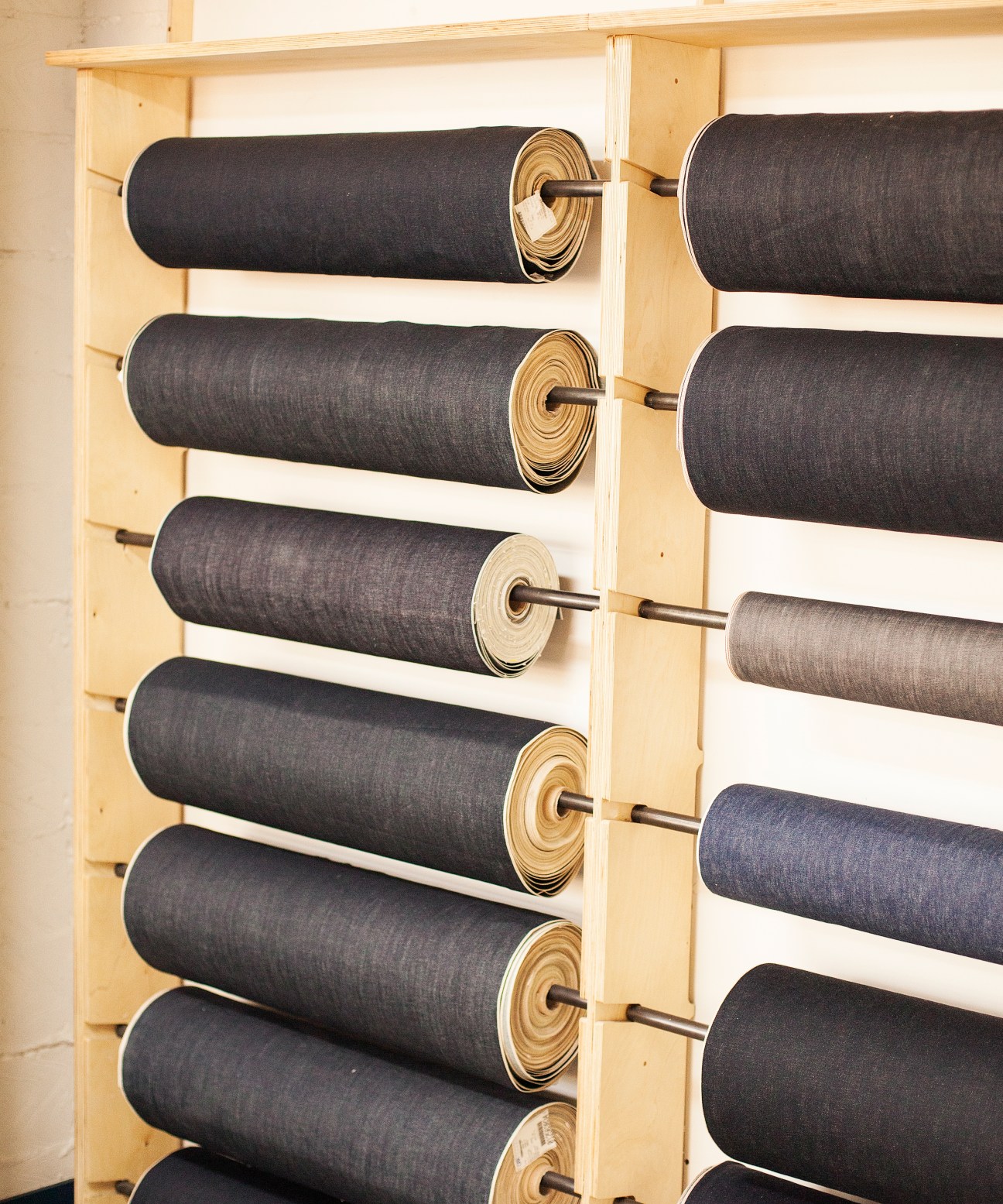 Rolled fabric swatches in black and neutral tones displayed on wooden dowels mounted on a light wood shelving unit.