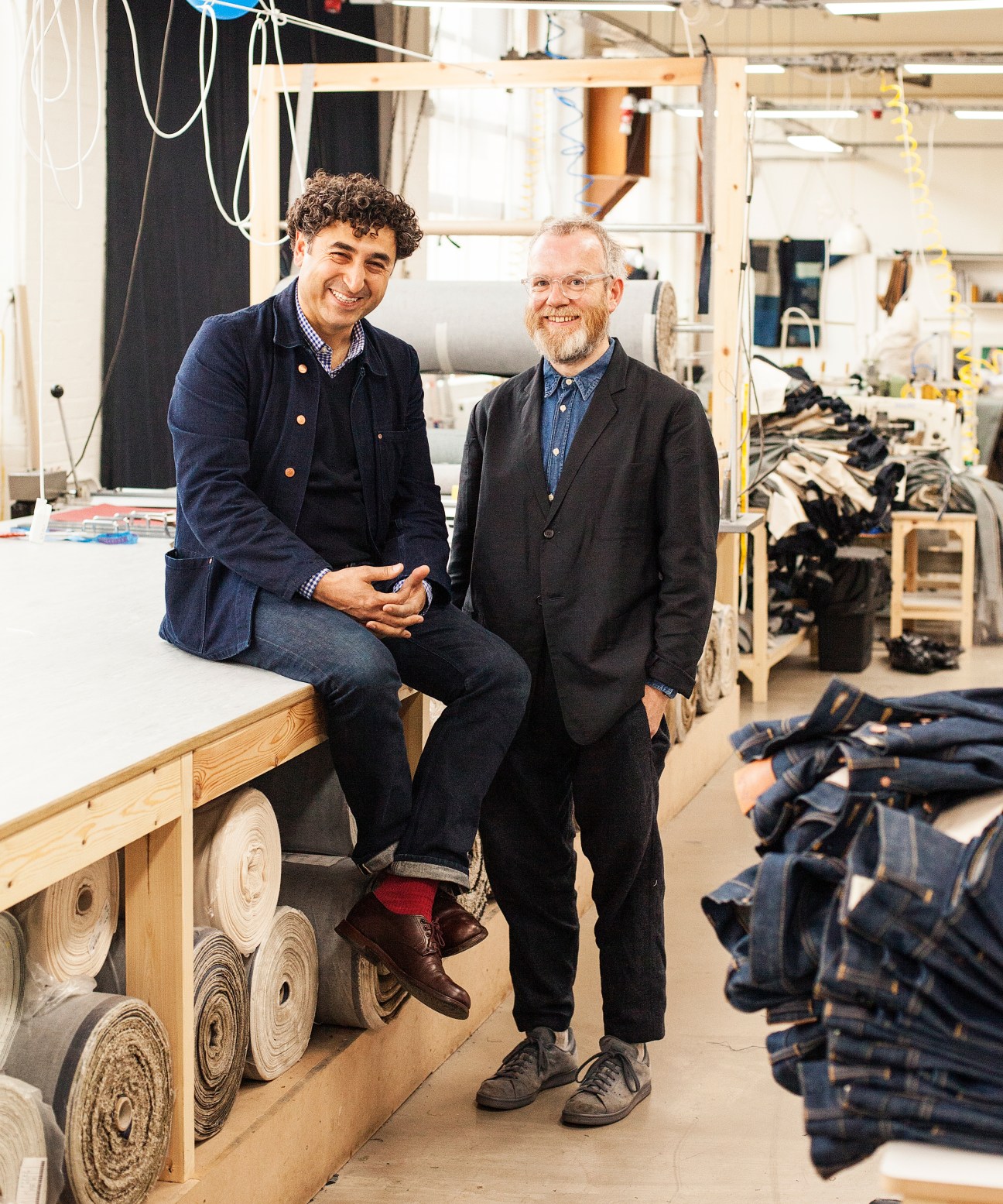Han Ates and Toby Clark, founders of Blackhorse Lane Ateliers, smiling in their jeans factory with machinery and denim in background.