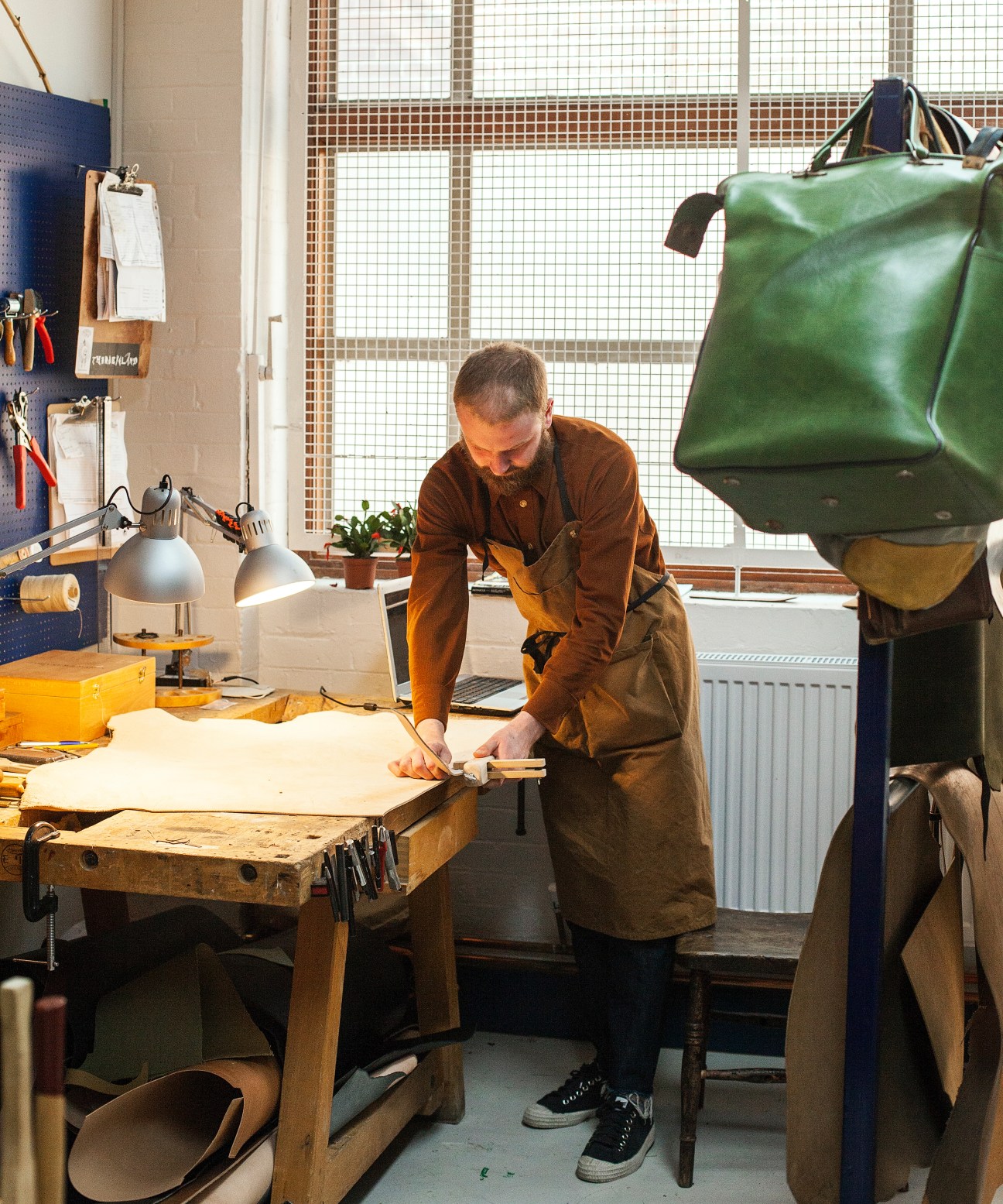 Leather craftsman Jonatan Staniec works at a wooden table in his rent-free workshop space at Blackhorse Lane Ateliers factory.