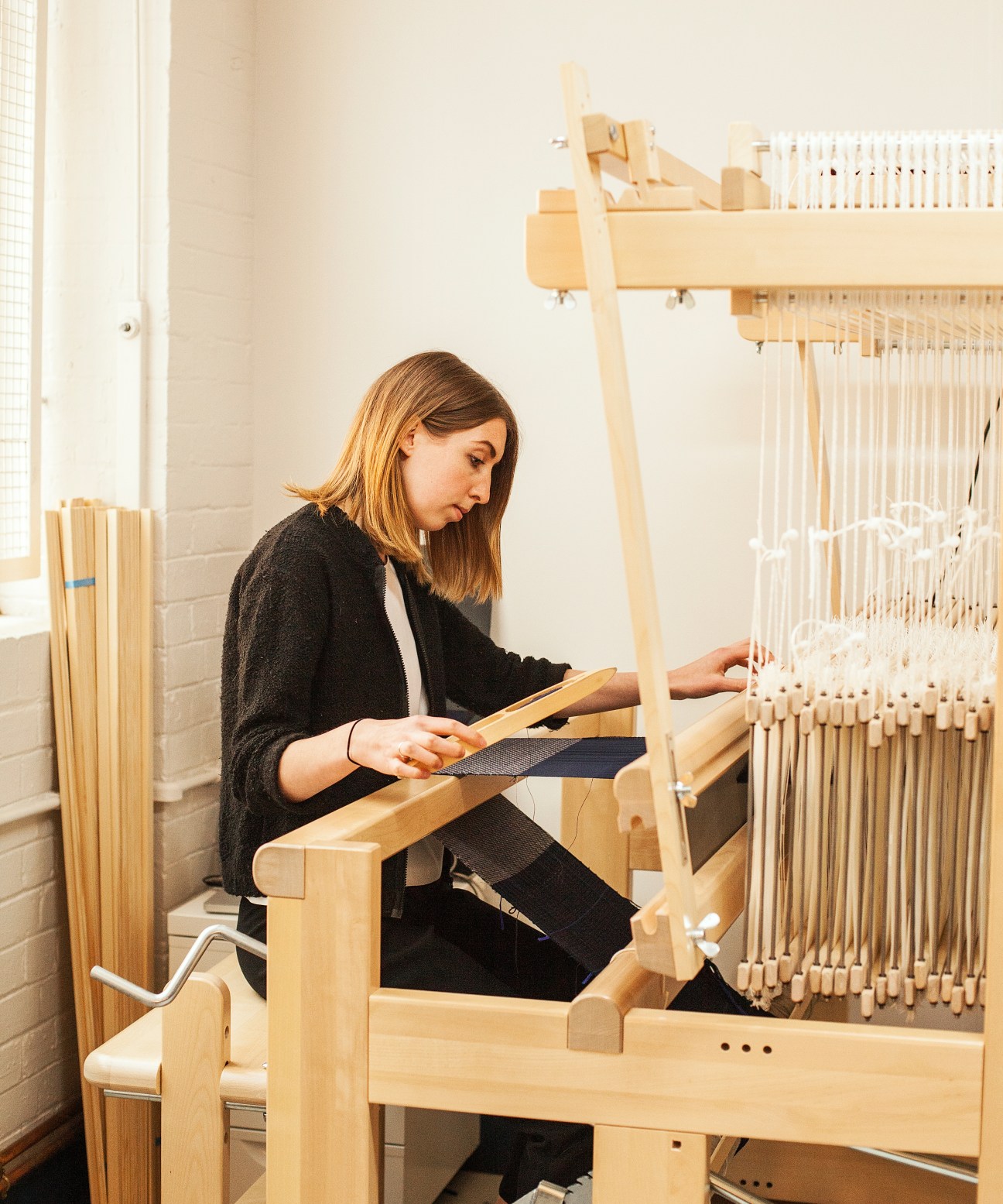 Textile weaver Sophie Reeves working at a wooden loom with threads.