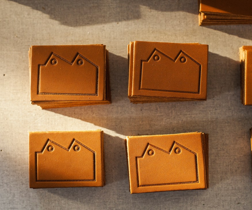 Four tan leather labels with embossed house-shaped designs and small holes, referencing Blackhorse Lane Ateliers' factory façade.