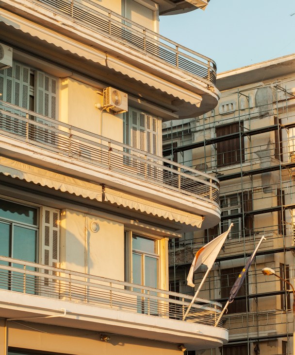 Mid-century curved building facade with cream-colored concrete, metal railings, and retractable awnings on Nikis Avenue in Thessaloniki.