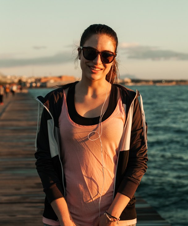 Woman jogging along Thessaloniki's seafront promenade at sunset wearing earphones.