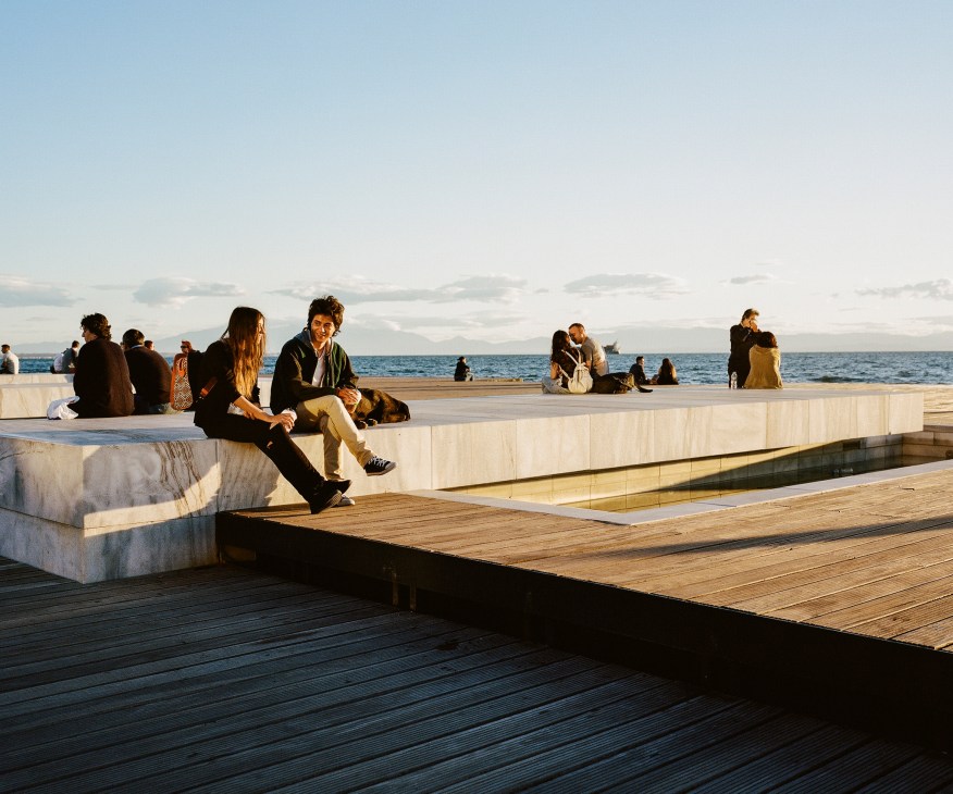 People sitting on white concrete waterfront seating overlooking the sea in Thessaloniki