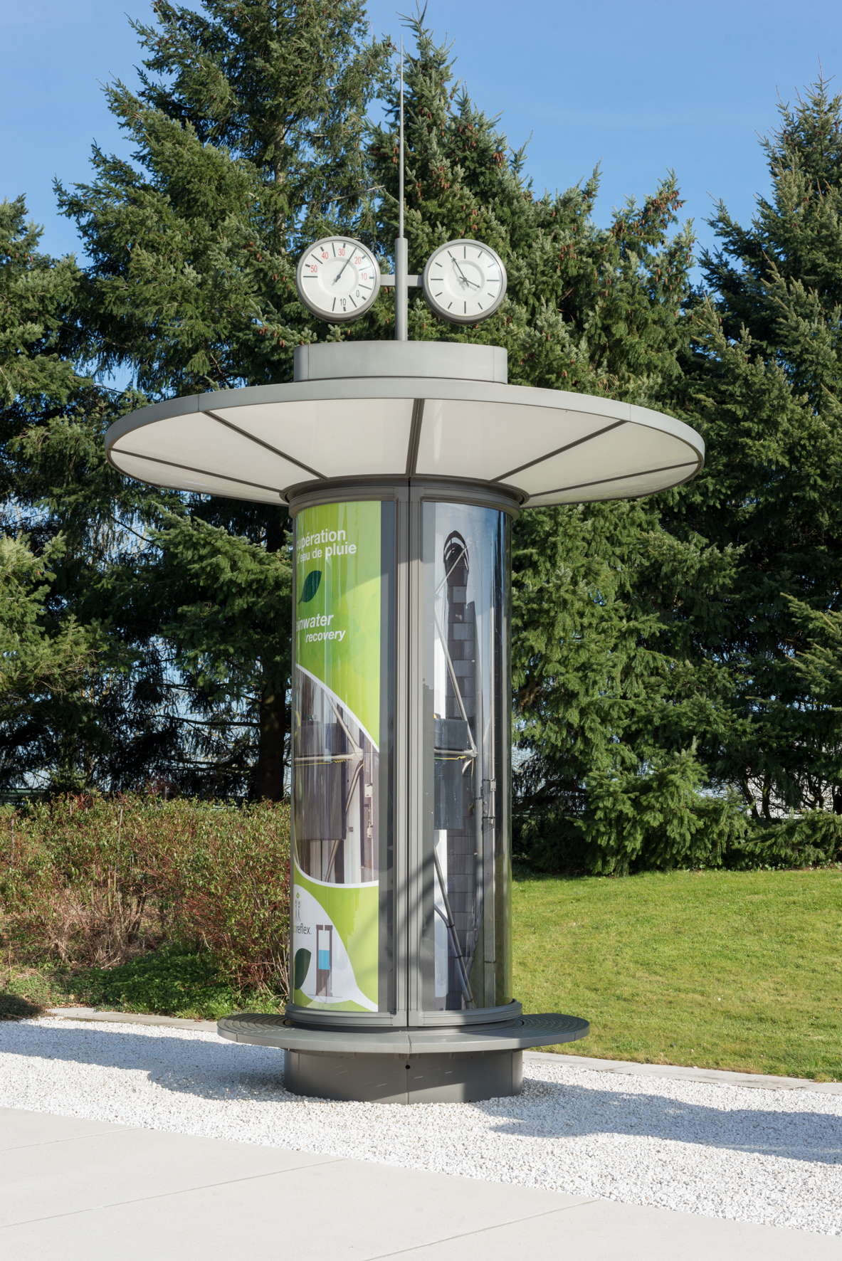 Cylindrical street furniture column with wide canopy top, two clocks, and advertising panels, designed by Norman Foster.