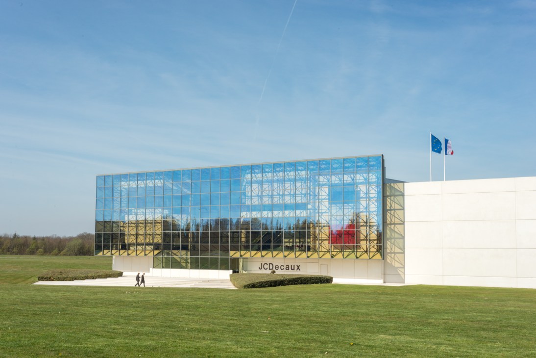 Modern glass and concrete JCDecaux head office building with flags on a grassy landscape near Versailles.