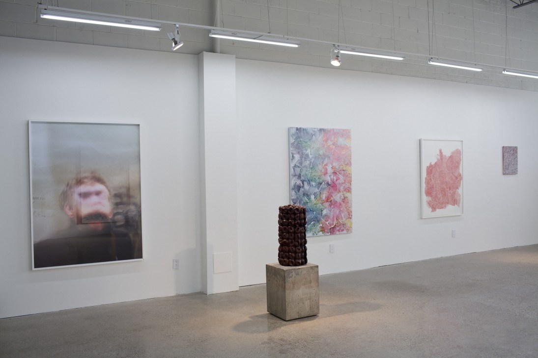Modern gallery interior with white walls, concrete floor, framed artworks, and a sculptural piece on a pedestal.
