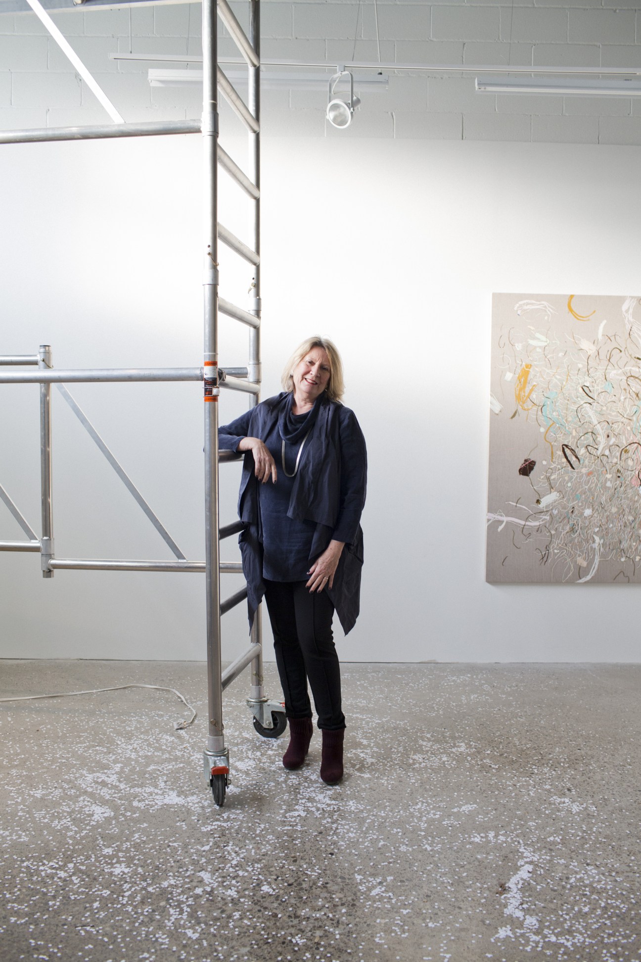 Jessica Bradley stands in her gallery space with white walls and metal scaffolding.