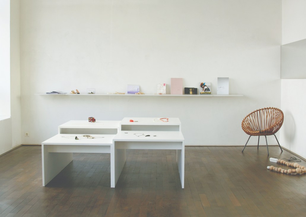 Minimalist jewelry shop interior with white display tables, floating shelf, and woven chair.