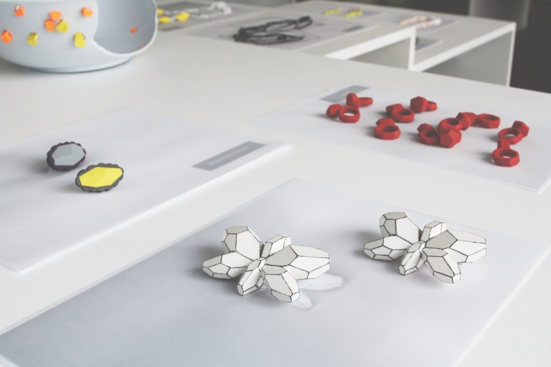 Oona jewellery pieces displayed on white surface including geometric white polycarbonate ornaments and red bangles.