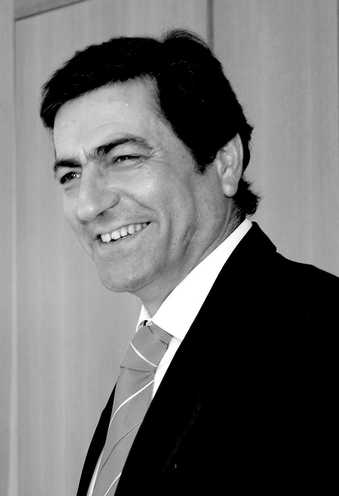 Black and white portrait photograph of João Goulão, a man in a dark suit and striped tie, smiling at the camera.