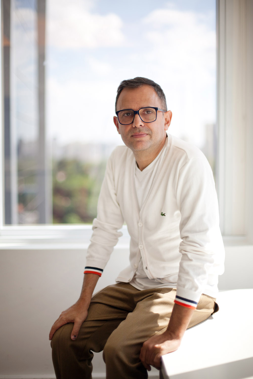 Paulo Borges, founder of São Paulo Fashion Week, sitting by a window overlooking the city skyline.