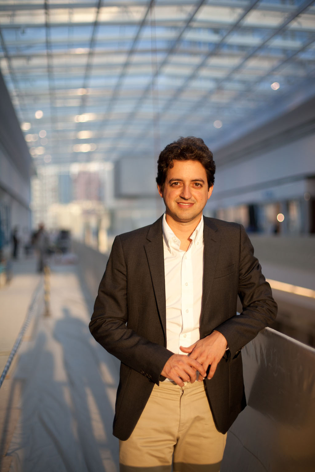 Carlos Jereissati Filho stands in a modern glass-ceilinged mall atrium wearing a dark blazer and light pants.