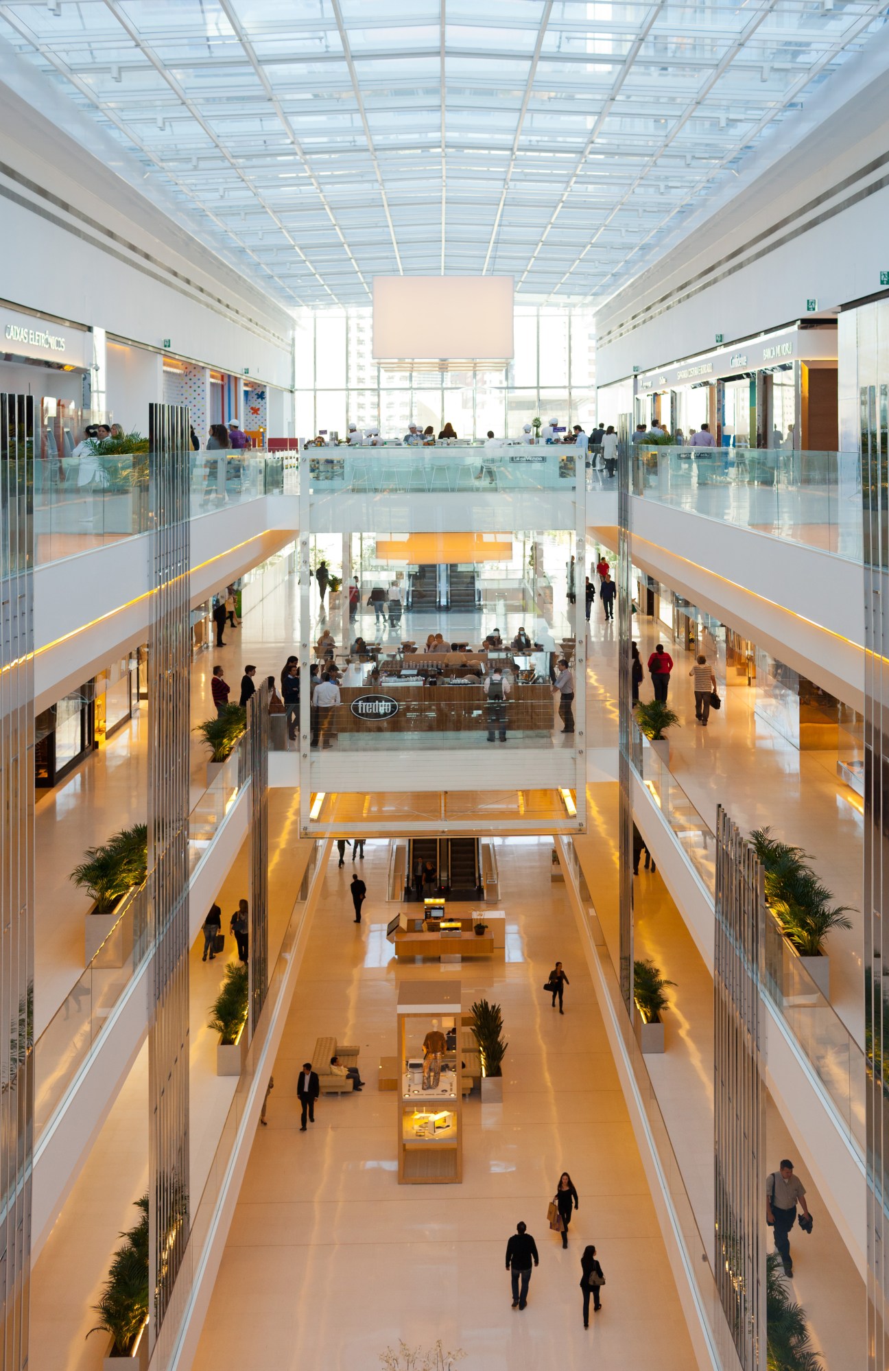 Main atrium at JK Iguatemi mall with multiple levels, glass railings, skylights and shoppers.