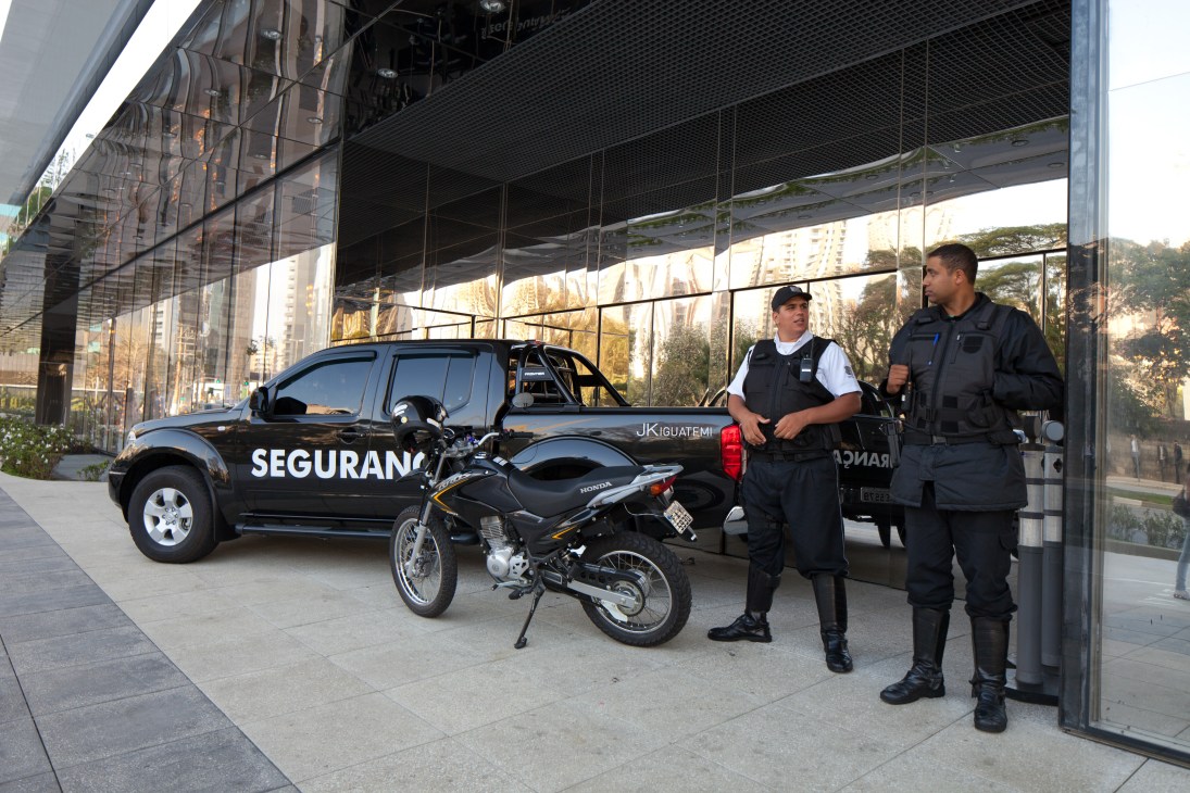 Security personnel stand outside JK Iguatemi mall with a security vehicle and motorcycle in São Paulo.