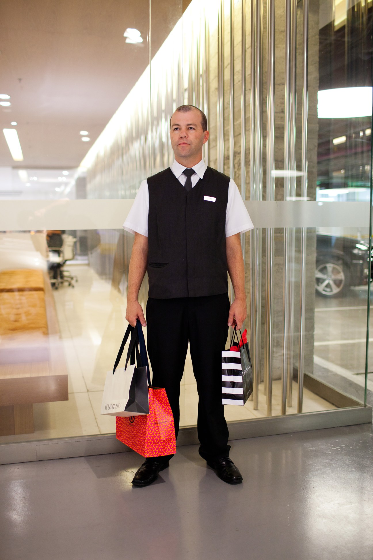 Uniformed mall security staff member holding shopping bags in a modern mall corridor.