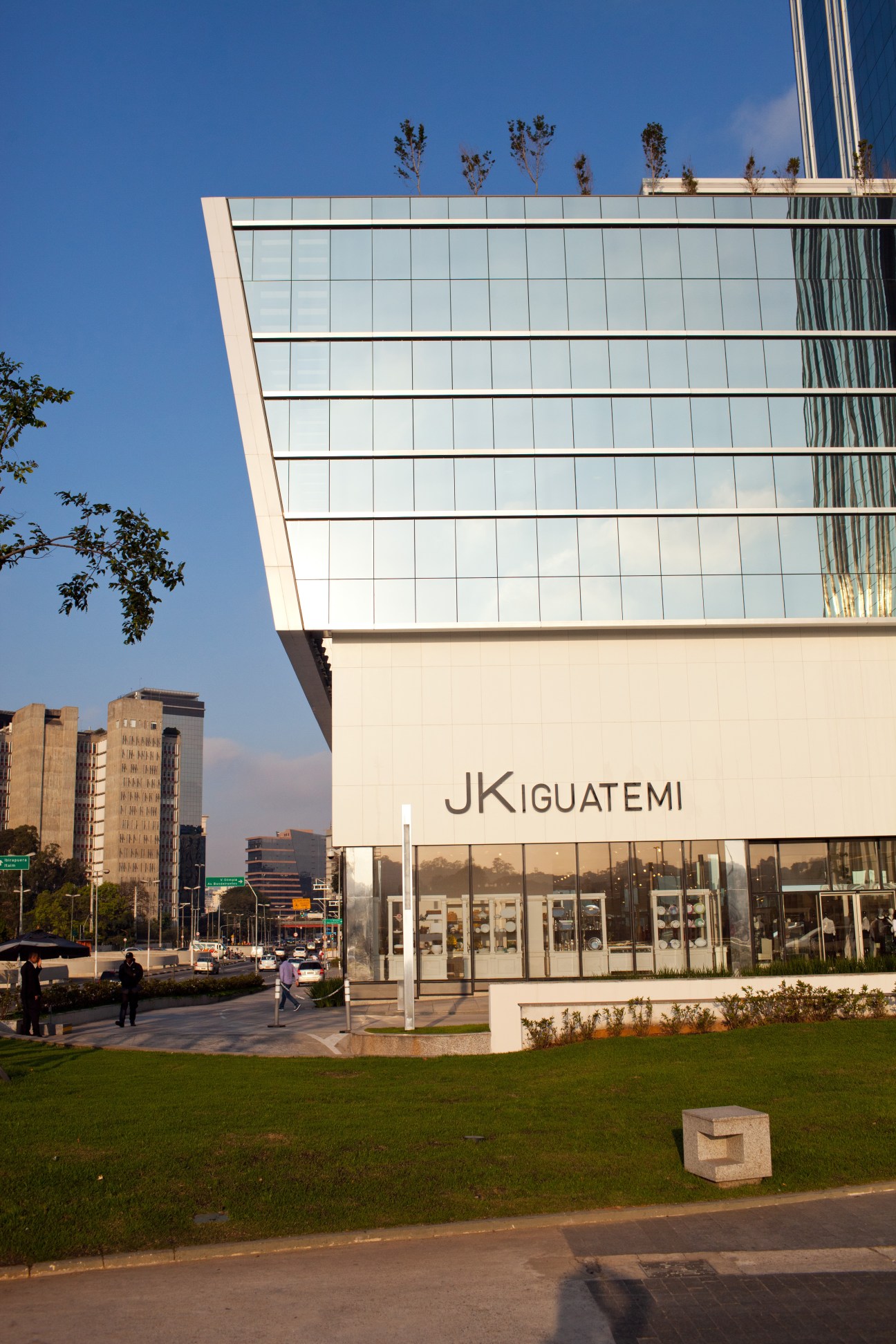 Modern glass and white facade of JK Iguatemi shopping mall with São Paulo cityscape in background.