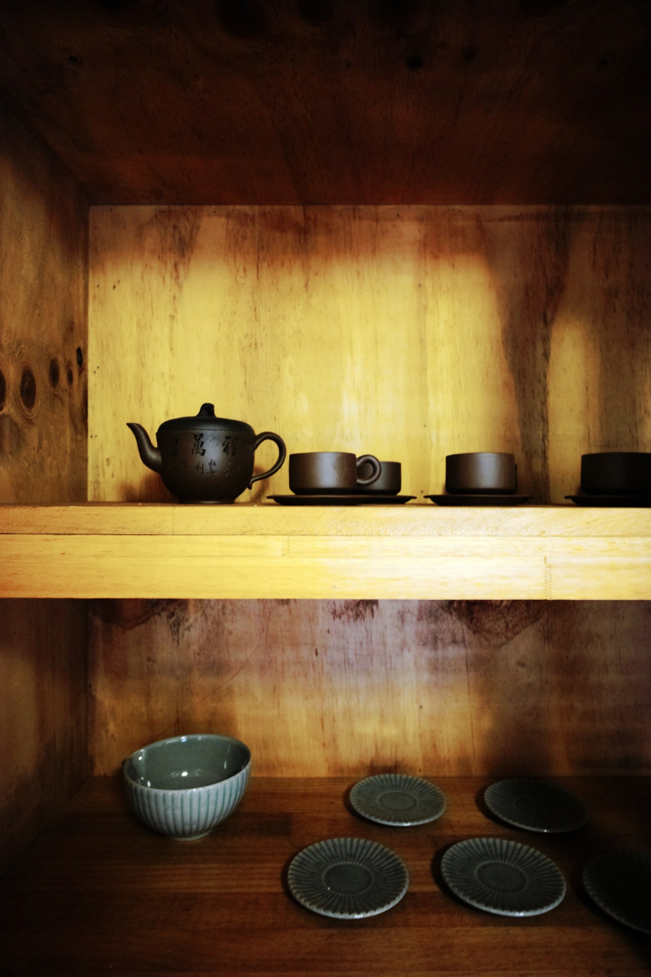 Tea service items displayed on wooden shelves in a traditional Korean hanok cupboard.