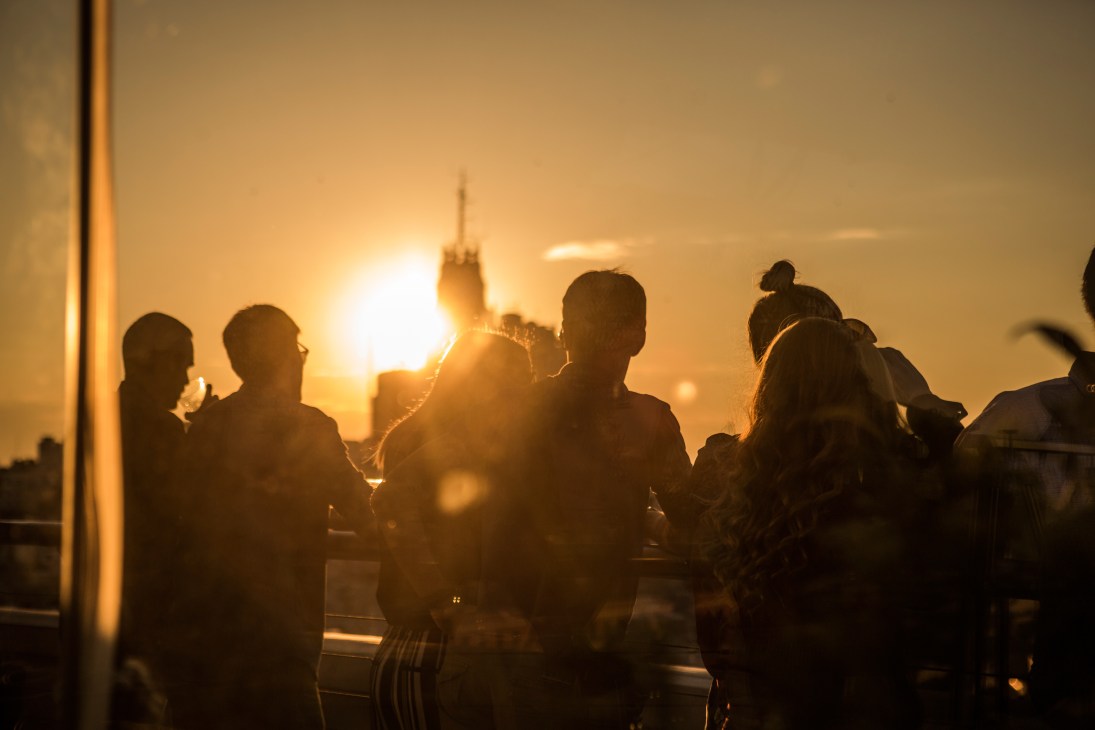 Silhouetted figures on a rooftop terrace at sunset with Madrid's Círculo de Bellas Artes visible in the golden light behind them.