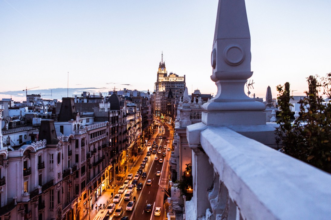 View from The Principle hotel rooftop bar overlooking Madrid's Gran Vía at dusk with illuminated buildings and street traffic.
