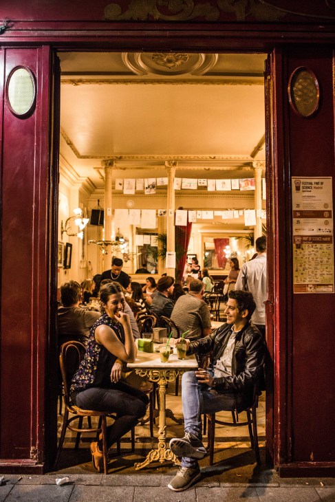 Patrons enjoying drinks at art nouveau Café Manuela, viewed through the red-framed doorway.