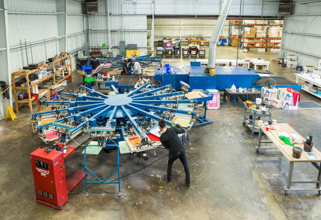 Worker operating large blue carousel screenprinting machine at The Icebox factory in Atlanta.