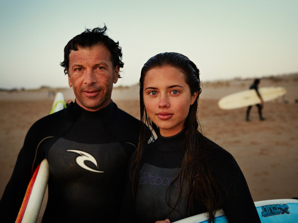 Two surfers in wetsuits holding surfboards on a beach.