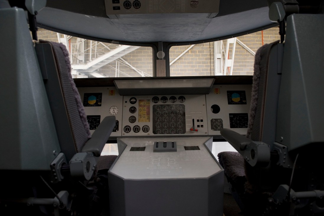 Interior view of airship pilot cockpit with instrument panels, controls, and windows overlooking hangar.