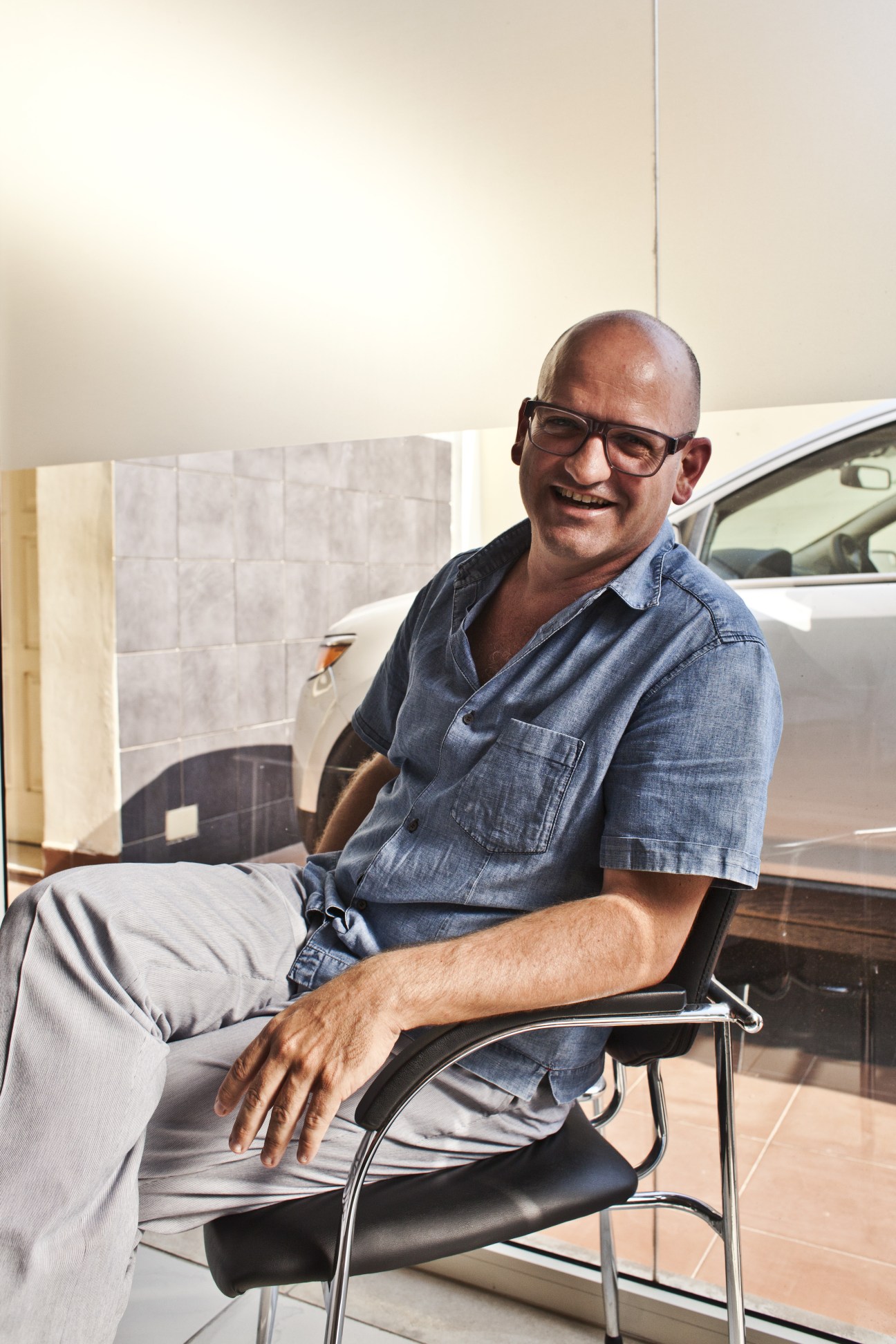 Jose Machado, an architect from Porto, sits smiling in a chair in an indoor space with a car visible behind him.