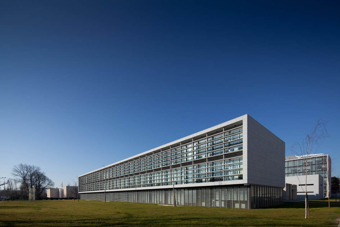 Modern multi-story building with anodised-aluminum façade and horizontal window bands set in a grassy landscape.