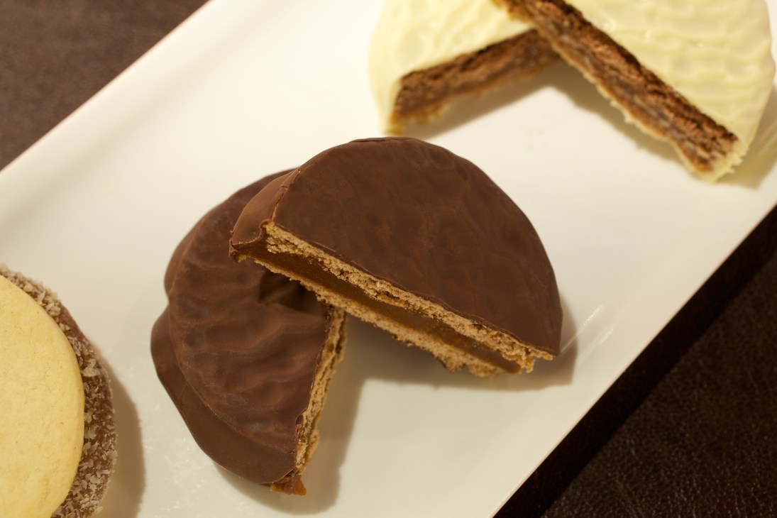 Cachafaz alfajor cut in half showing dulce de leche filling between buttery biscuits and chocolate coating.